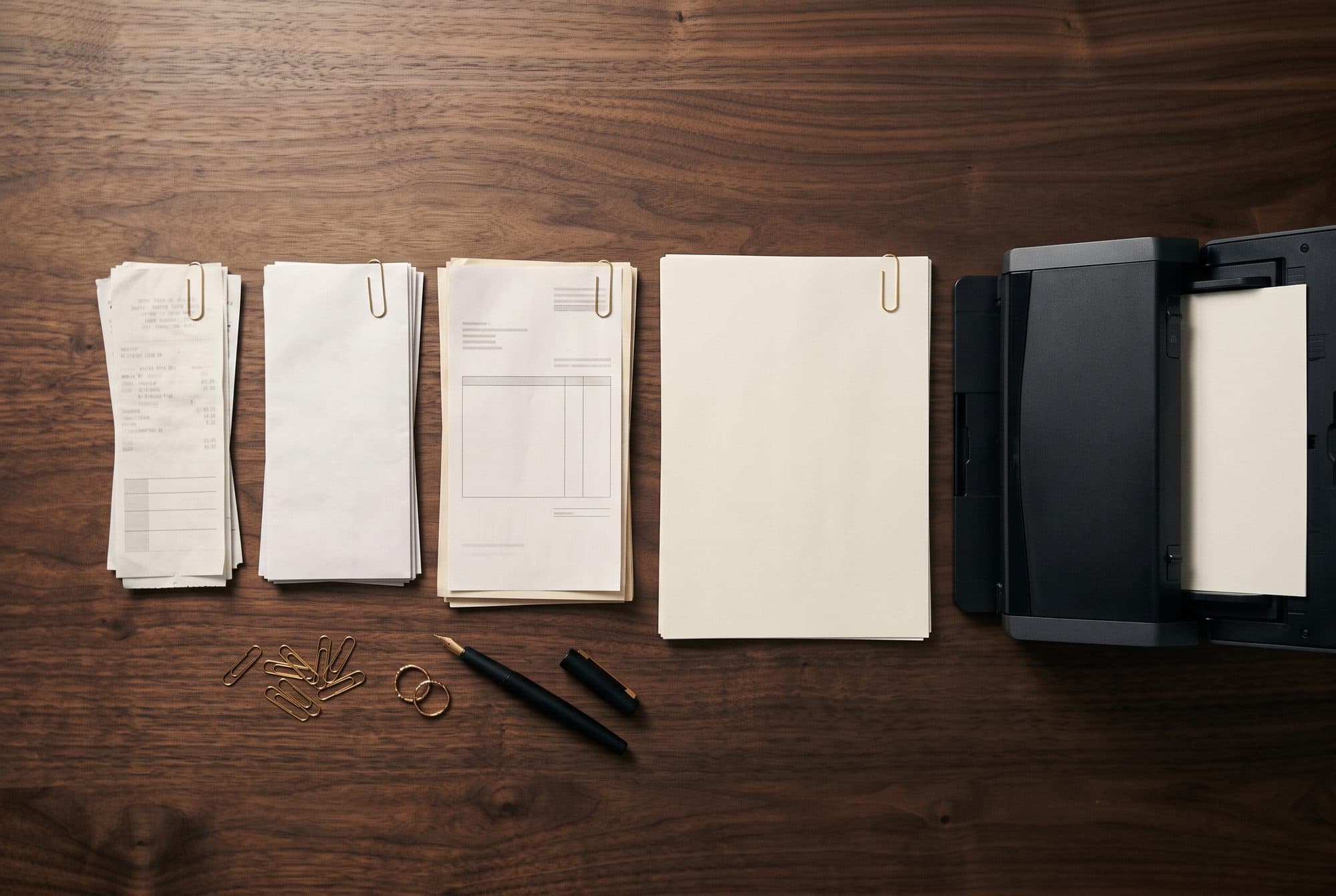 Bonnetjes en facturen in nette stapeltjes gesorteerd, elk met een gouden paperclip, naast een documentscanner.